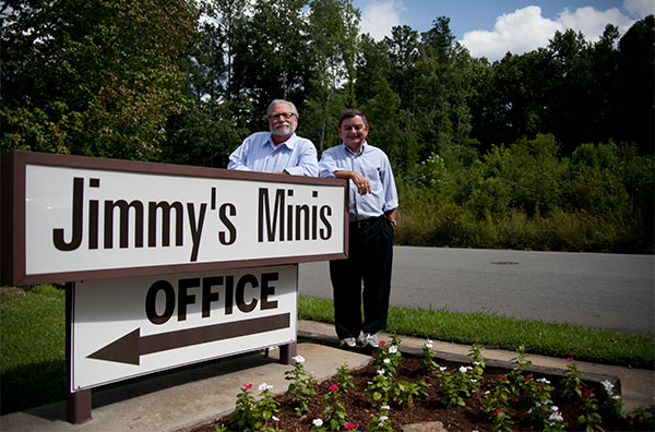 Two men standing next to a sign that says " jimmy 's minis office ".